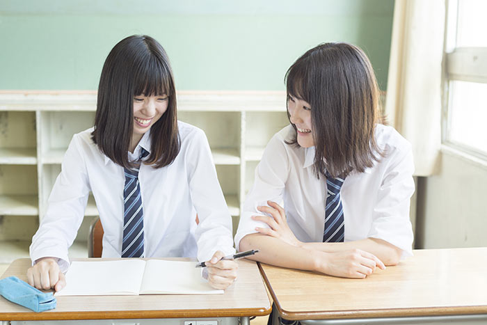 学校の隣どうしの机で話をする女友達