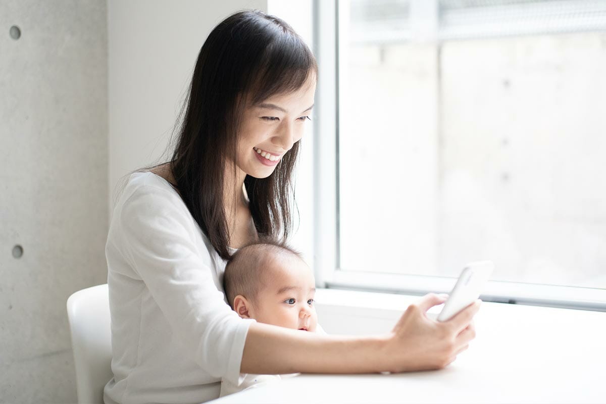 赤ちゃんを抱っこしてスマホを見ている笑顔の母親