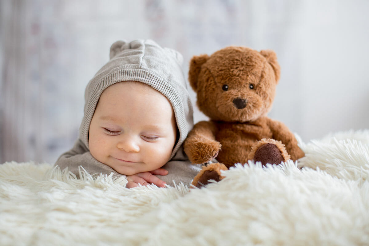 クマのぬいぐるみと眠るグレーのフードをかぶった赤ちゃん