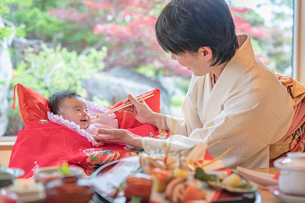 百日祝いのお食い初めで赤ちゃんの口元にご飯を持って行っている女性