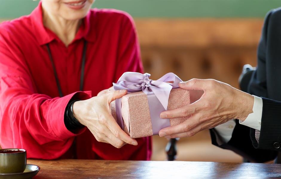 赤い服を着た女性に還暦祝いプレゼントを手渡している男性